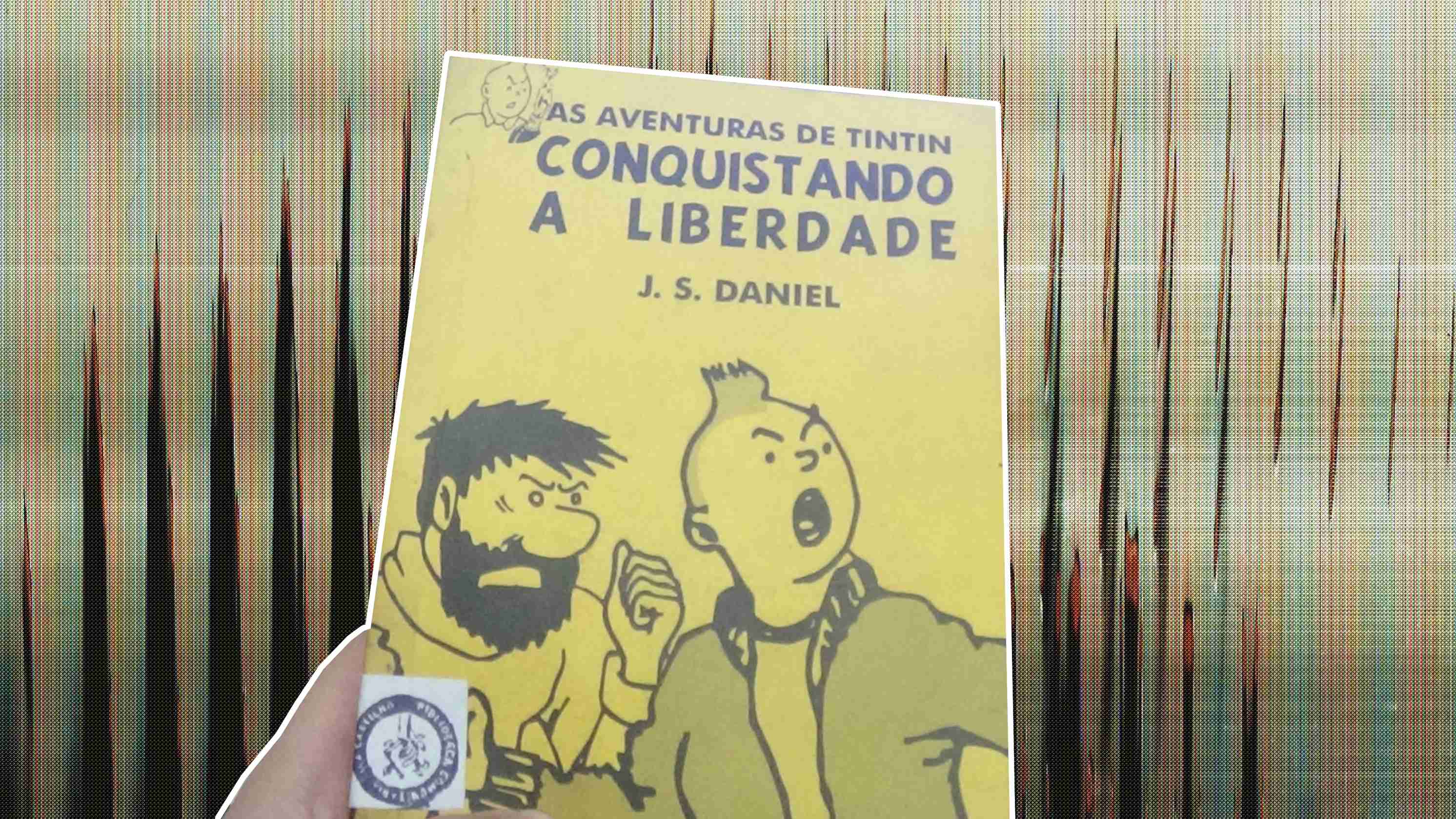 Foto editada de uma pessoa segurando o quadrinho do tintin conquistando a liberdade, a capa é amarela e possui o tintin gritando ao lado do capitão baddock barbudo serrando o punho. Abaixo do título grande As Aventuras de Tintin Conquistando a Liberdade, é possível ver o nome do autor J. S. Daniel