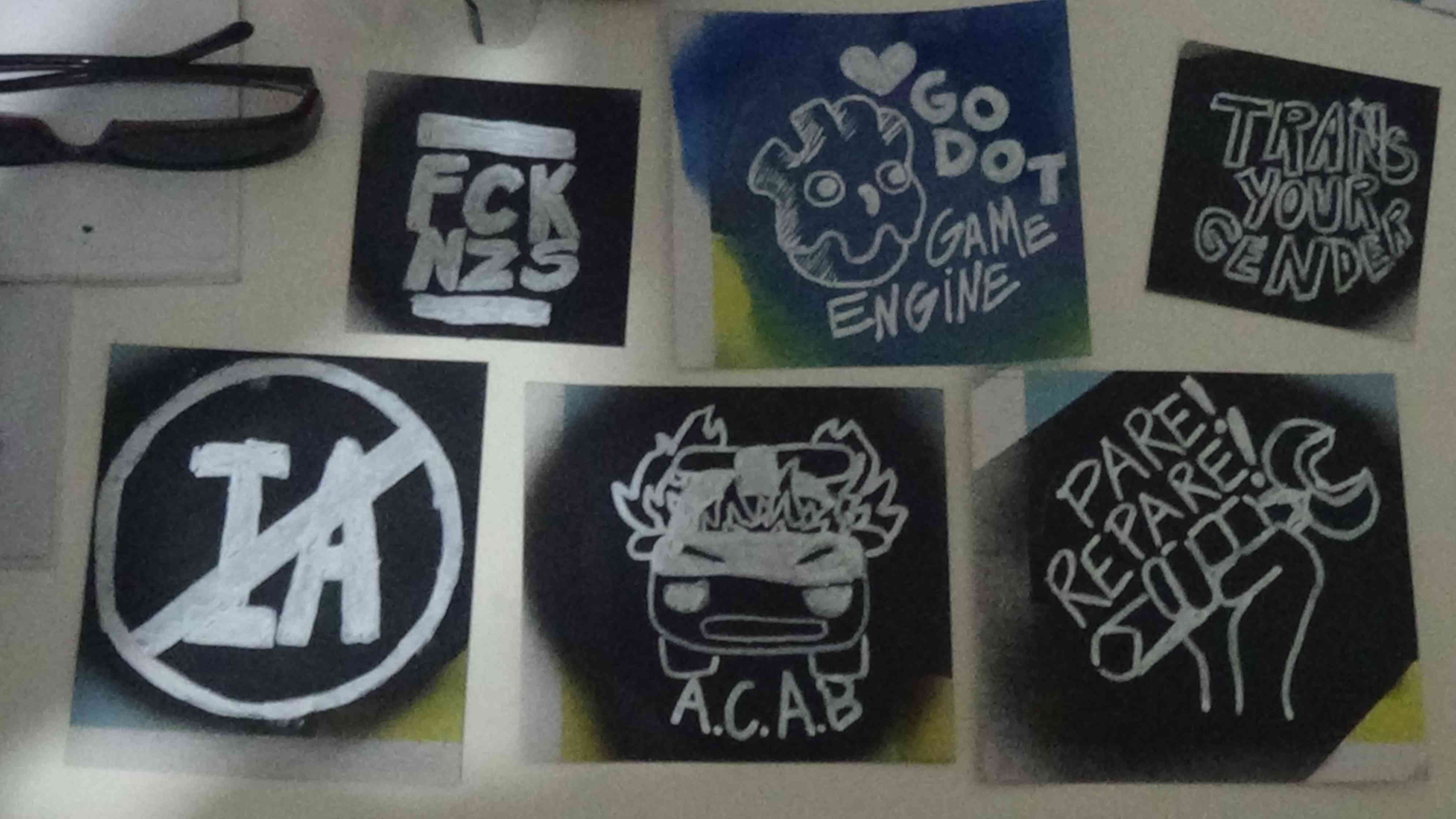 Foto de 6 adesivos prontos: 1 FCK NZS, 2 <3 Godot Game Engine, 3 Trans your gender, 4 Anti-IA, 5 Viatura pegando fogo ACAB, 6 Pare! Repare! Punho cerrado segurando uma ferramenta.