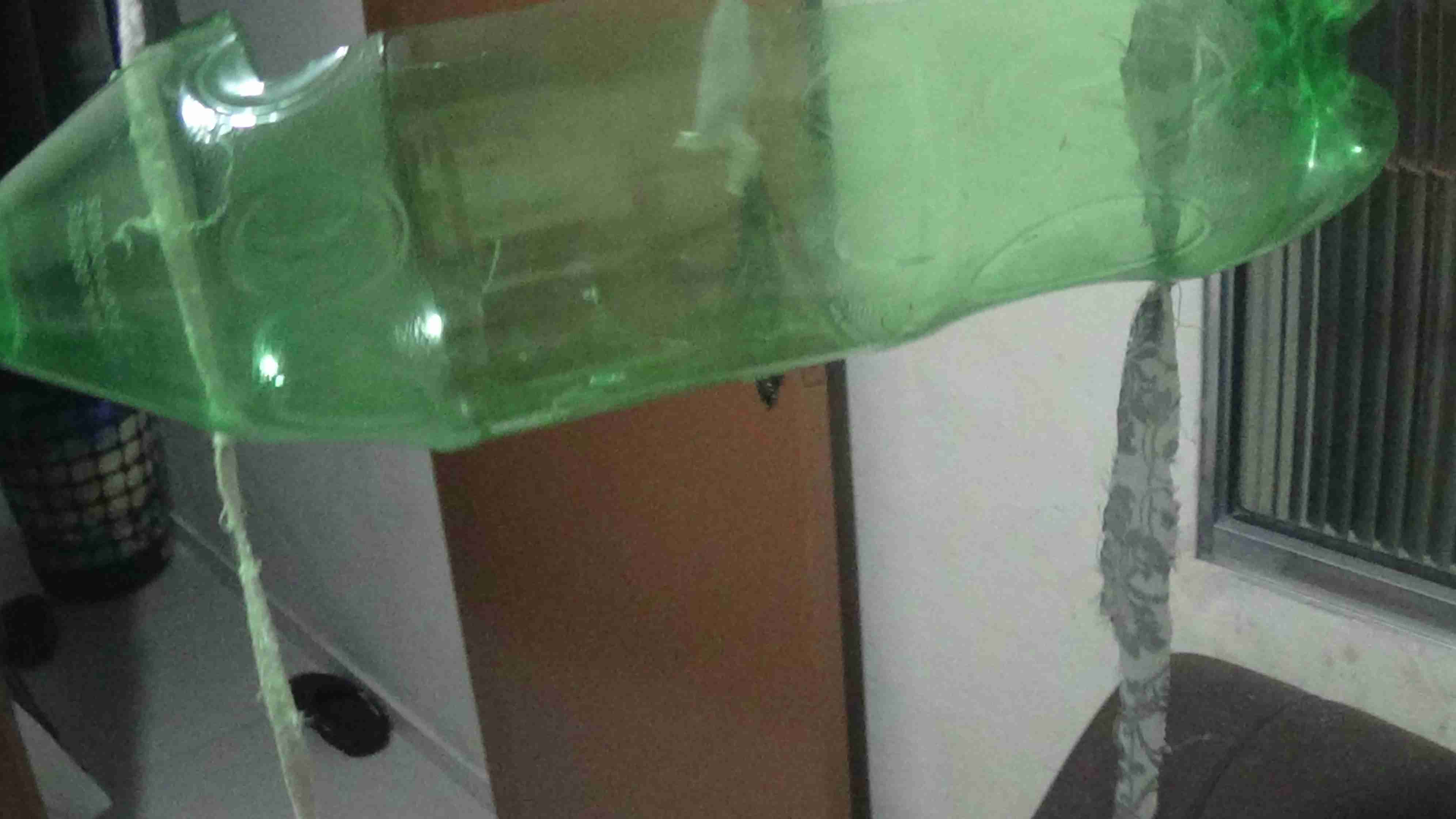 Garrafa pet na horizontal sendo atravessada por 2 fios, é possível ver os nós abaixo do furo, que sustentam a garrafa para não cair.