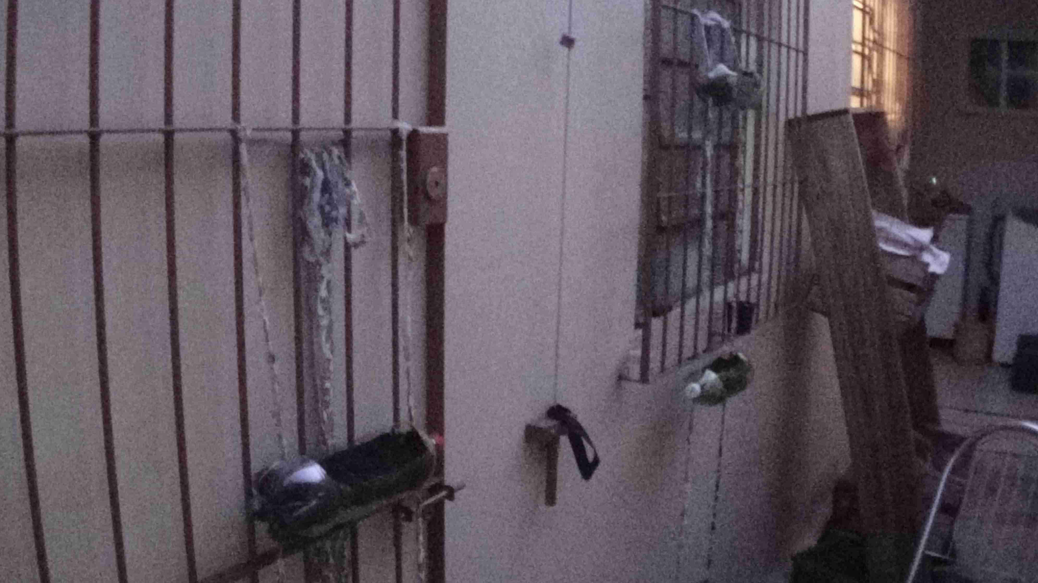Parte externa de uma casa onde é possível ver duas hortas verticais de garrafas pets penduradas em grades pelos dois fios que são entrelaçados na grade e amarrados, garantindo a sustentação.
