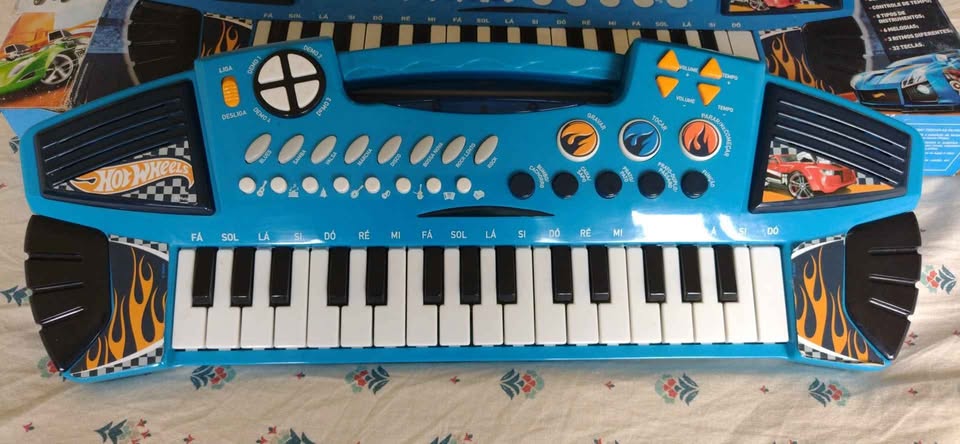 Foto do Teclado da Hotwheels, é azul com labaredas de fogo nas laterais, possui um teclado e ao redor vários botões com nomes para suas funcionalidades.